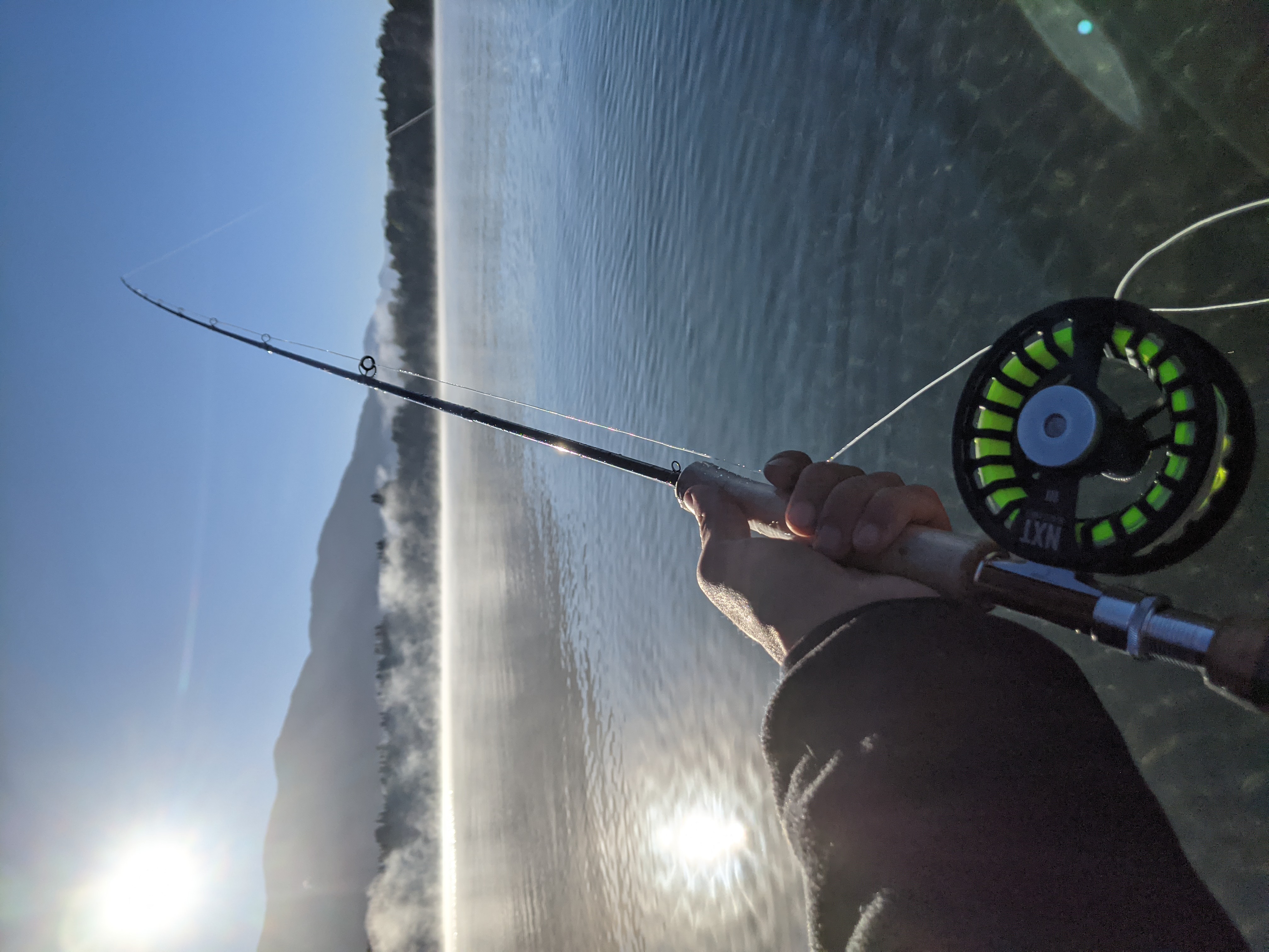Pesca con mosca al amanecer sobre un lago calmo con niebla y montañas al fondo