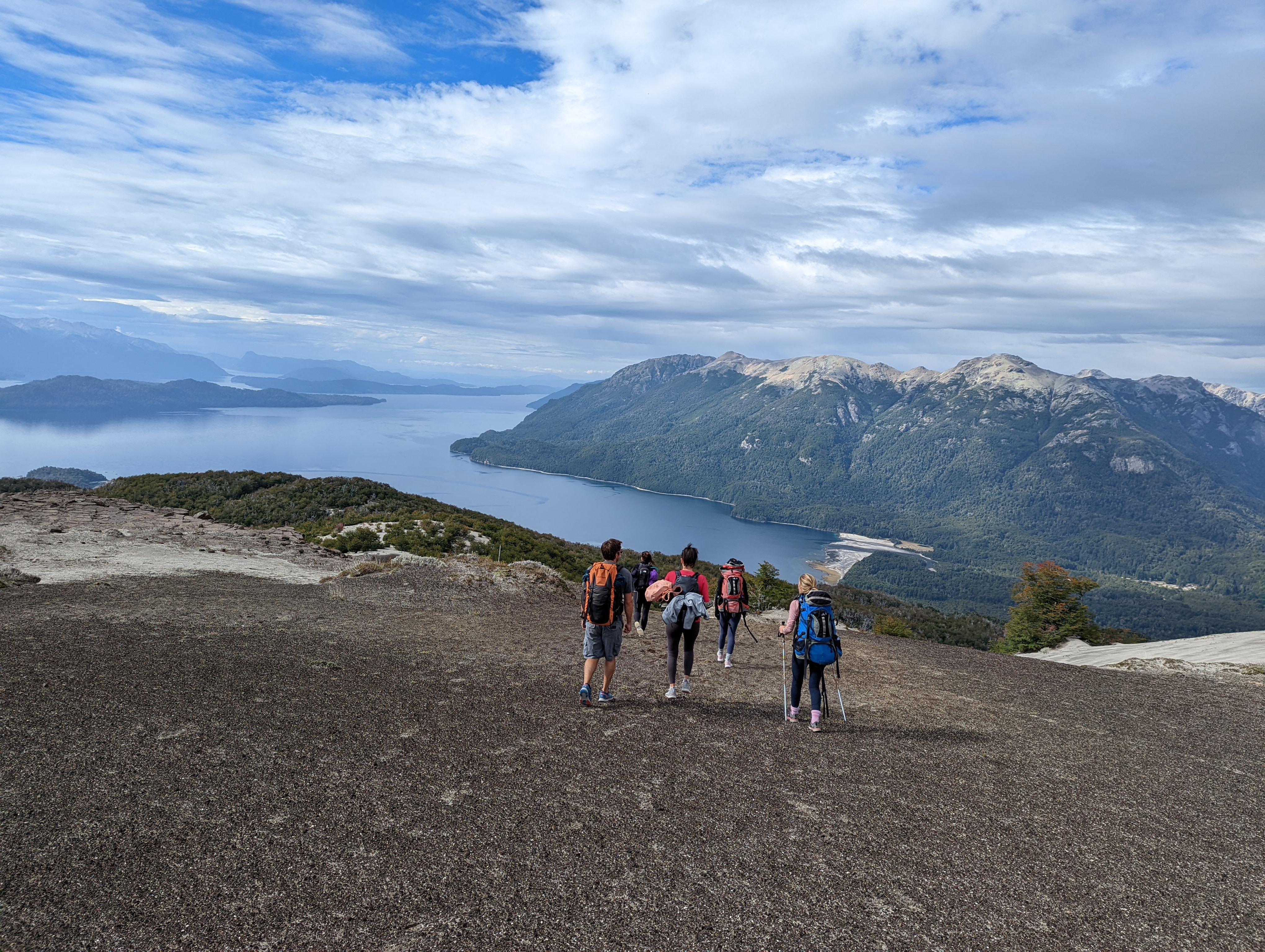Grupo de senderistas con guía descendiendo un cerro con vista panorámica al lago